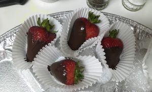 4 chocolate dipped strawberries in small paper cups set together on a glass plate.